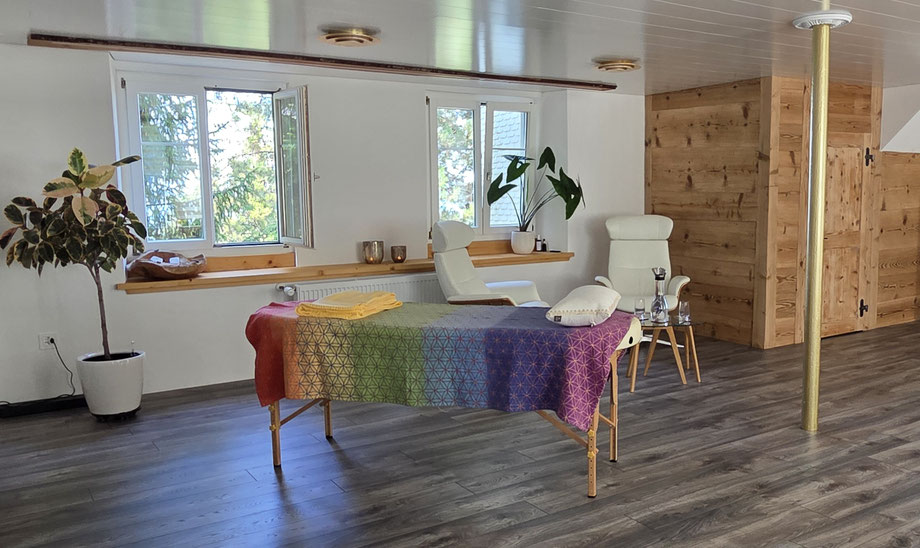 Heller, gemütlicher Praxisraum für Energie- und Chakra-Behandlungen in der Schweiz bei energievollsein. Natascha bietet hier berührungslose Sitzungen für Energie & Balance auf einer Massageliege mit farbiger Chakra-Decke an.