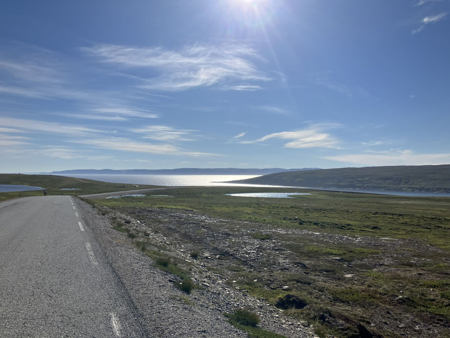 Bikepacking-Tour durch Finnmark – einsame Straße mit Radfahrer unter blauem Himmel