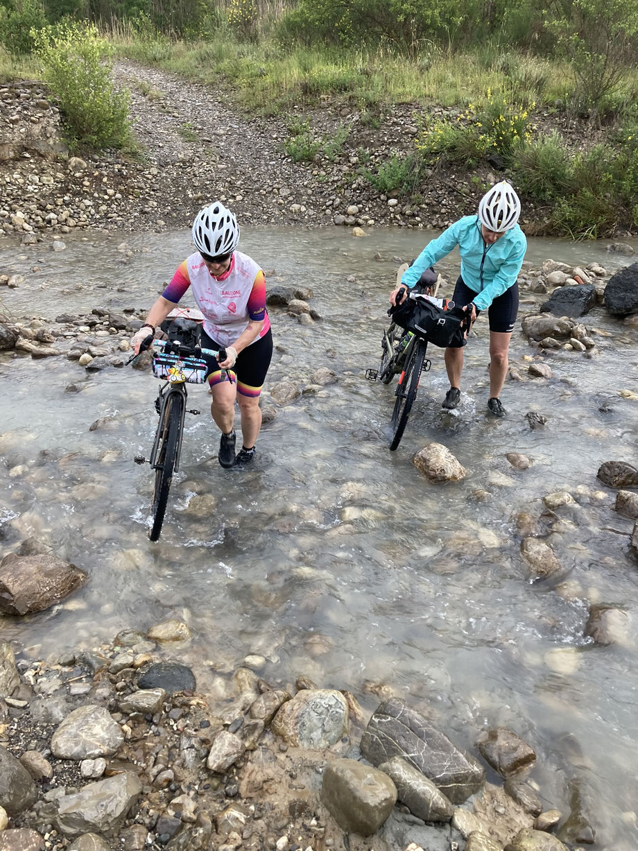 Gravel- und Bikepacking-Tour in der Toskana, zwei Radfahrerinnen durchqueren eine Furt.