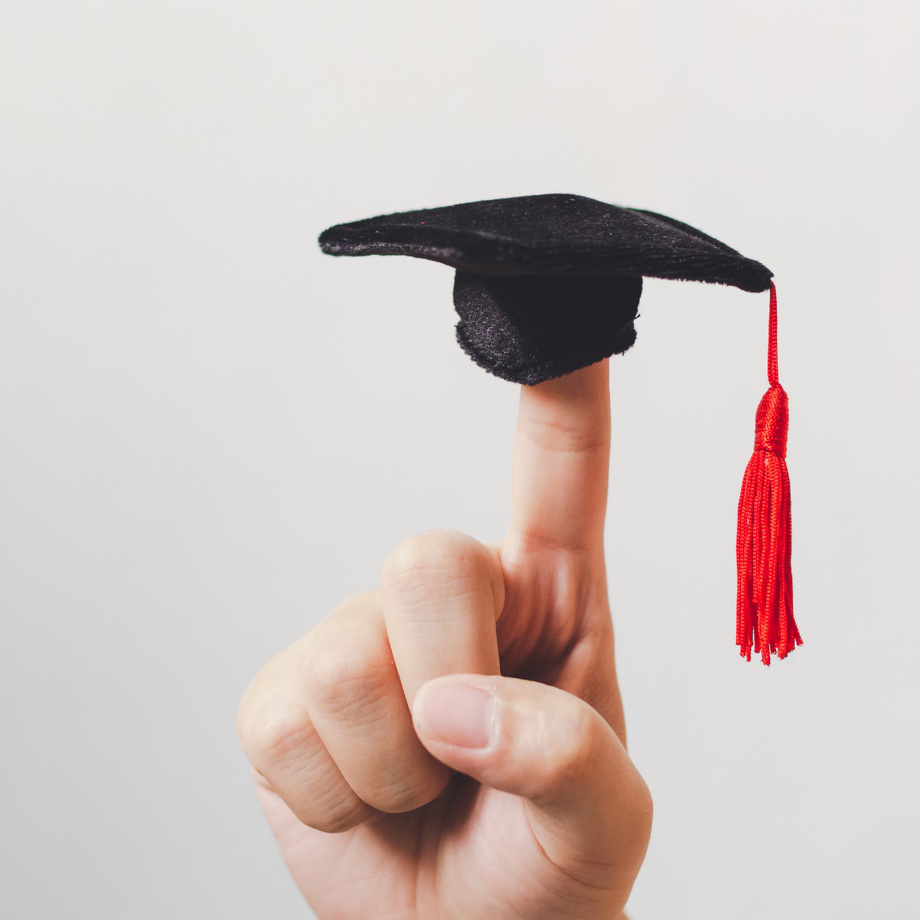 Hand mit ausgestrecktem Zeigefinger, auf dem ein Fingerhut sitzt, der einen Studienhut darstellt