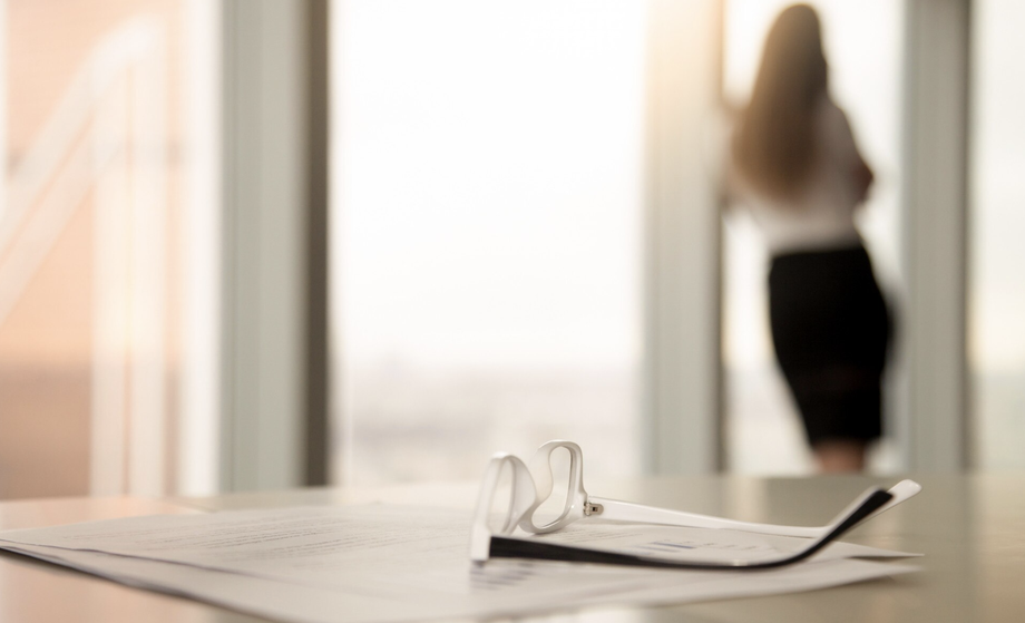 Arbeitsvertrag mit Brille im Vordergrund, unscharfe Frau am Fenster im Hintergrund – Symbolbild für verhaltensbedingte Kündigung und Datenschutz