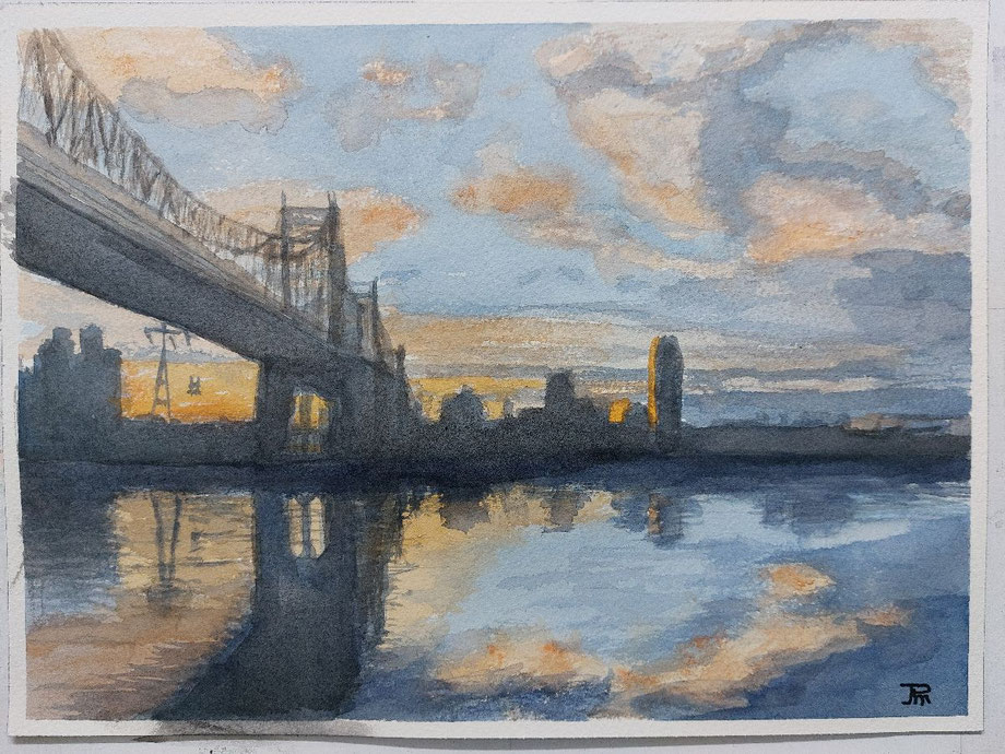 Puente colgante sobre el agua con reflejos cálidos del atardecer y silueta urbana al fondo.