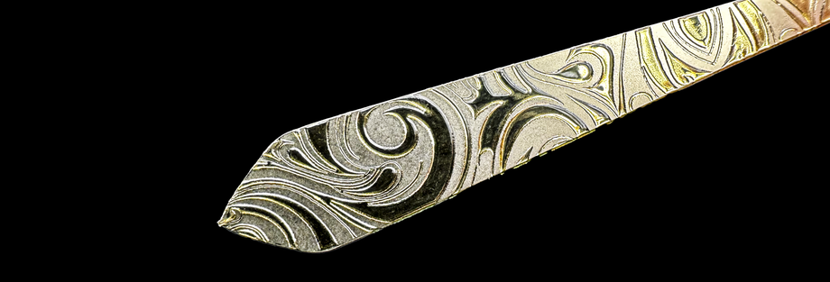 銀色の金属素材に、渦巻き状の立体模様が盛り上がって印刷された眼鏡テンプル。光の反射により凹凸感と陰影が際立ち、盛り上げ印刷の質感がはっきりとわかる。