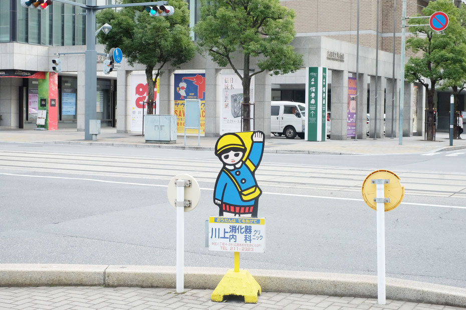 広島県立美術館前にある横断歩道に置かれた日静企画の広告看板まもりっこ
