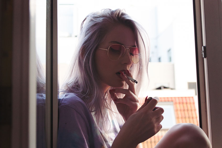 Model Astrid Heuker, smoking a cigarette in the window. Model is wearing aviatar sunglasses. Photographed by Landa Penders.