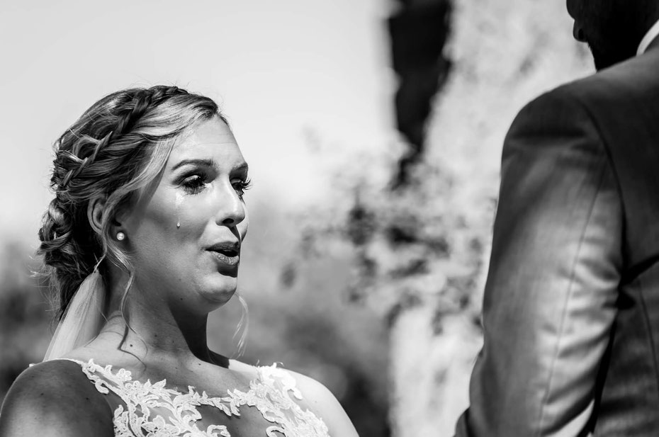 Black and white photo of a bride and groom. Bride is exhaling with a tear rolling down her cheek. Groom is visible from behind. 