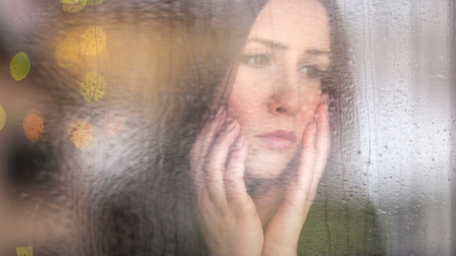 Frau steht hinter Glasscheibe und versteckt sich vor ihren Emotionen