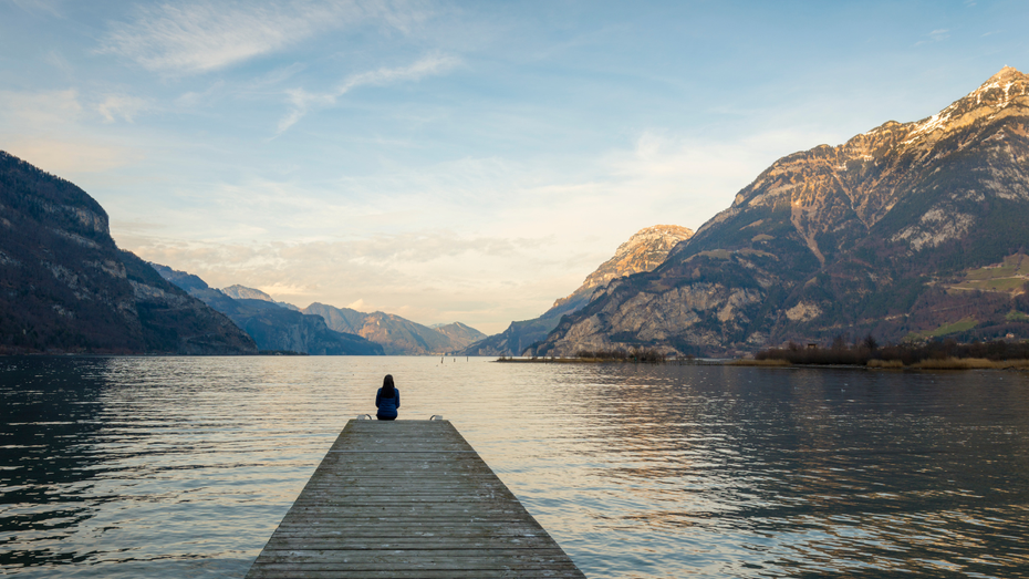 Frau sitzt am Steg vor einer wunderschönen Berglandschaft als Symbol für den Weg, der vor ihr liegt, wenn sie die Selbstverantwortung für ihren inneren Zustand übernimmt