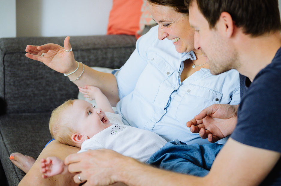 Ein fröhliches Baby liegt auf den Beinen der Eltern und lacht sie dabei an.