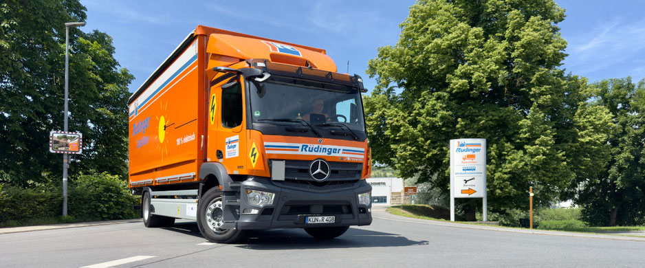 Viele orangene Lkw der Rüdinger Spedition stehen in einer Reihe nebeneinander. Vor ihnen steht vorne links ein weiterer Lkw.
