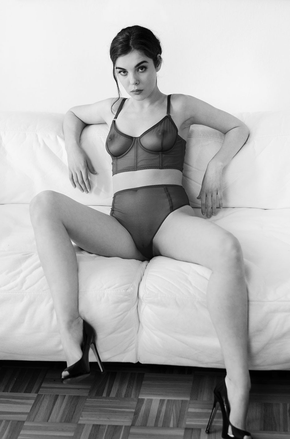 Nude model Dako Haux is sitting on a white leather sofa wearing lingerie