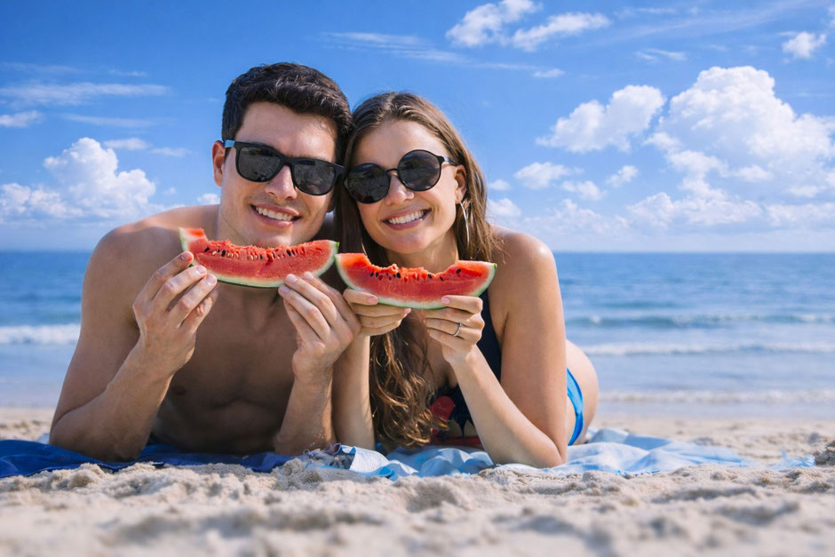 Pärchen am Strand mit Sonnenbrillen isst Melonen