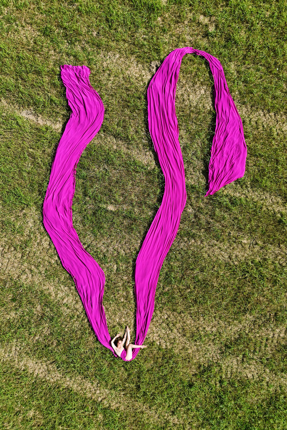 Drone photography of V3ruschka on grass with a huge magenta textile seemingly floating but actually lying on grass