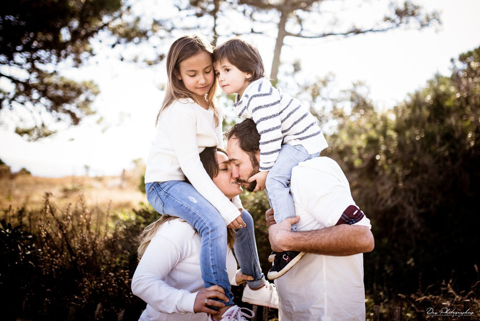 Parents kissing while carrying their children on their shoulders during a family photoshoot in Saint-Tropez.