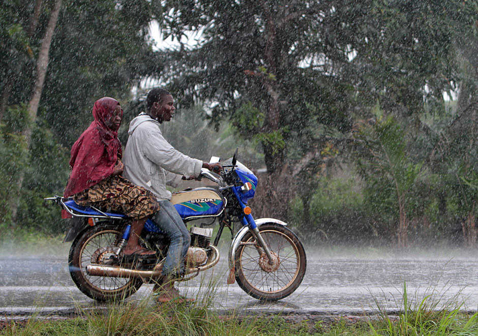 African motorists traveling couple Beninese motorcycle in the rain. Ouidah.