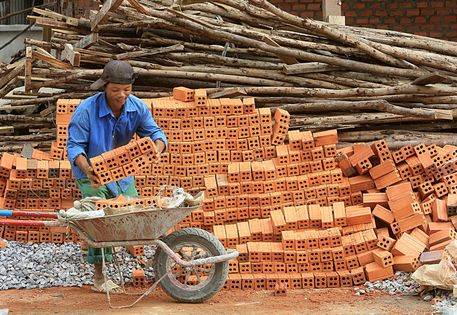 Ouvrier transportant des briques dans une brouette. Chantier de construction. Vang Vieng. Laos.