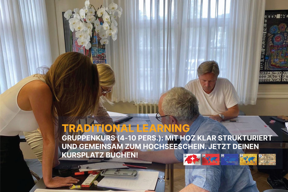 Drei Teilnehmende studieren Seekarten und Pläne an einem grossen Tisch in hellem Schulungsraum; gemeinsames Lernen im Gruppenkurs.