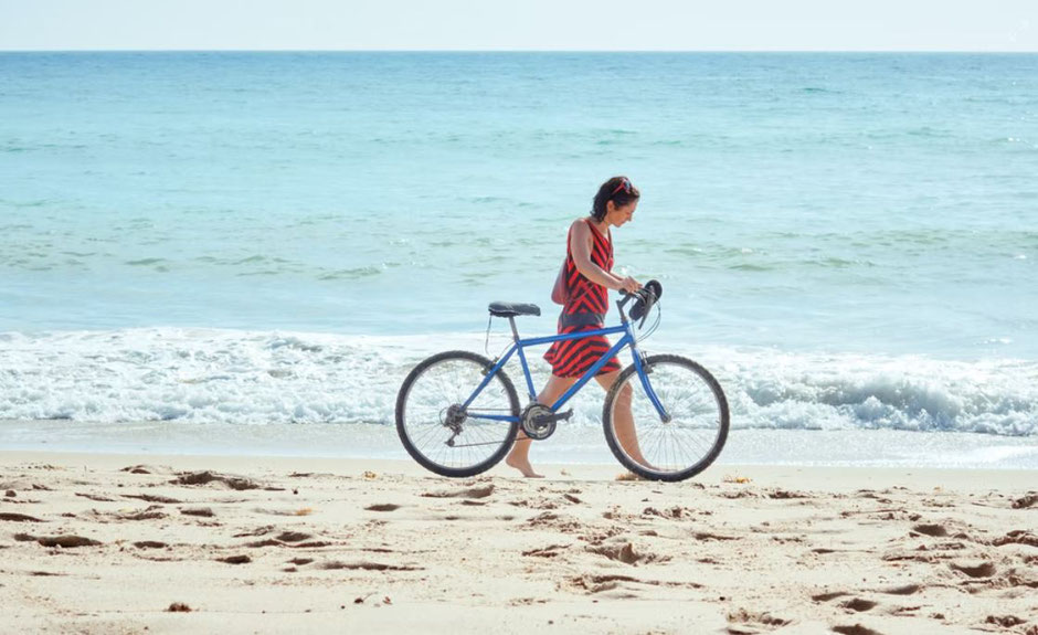 Femme poussant un vélo sur la plage