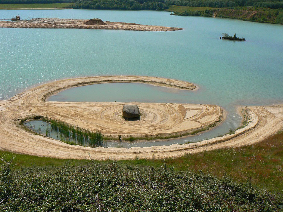 Sur un lac une spirale de sable avec un gros rocher noir au centre.#art#provence#ayniart
