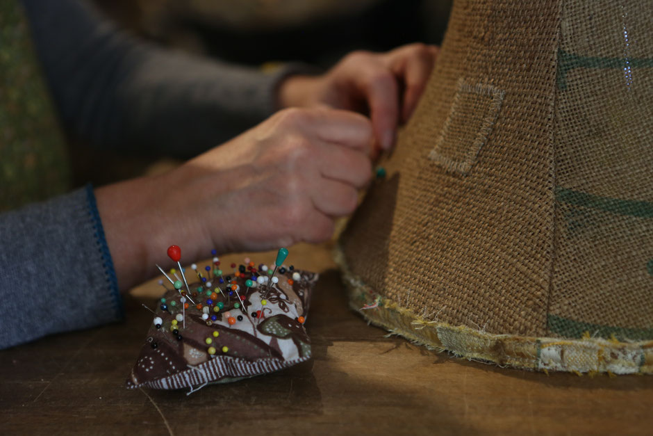 Main travaillant à l'aiguille sur une toile de jute recouvrant un tabouret tamtam