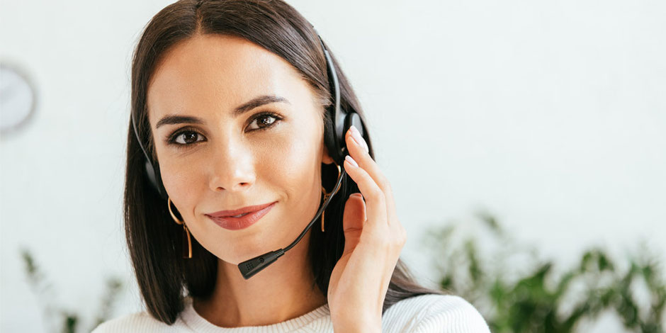 Portrait einer freundlich schauenden Mitarbeiterin mit Headset, die Anrufe entgegen nimmt.