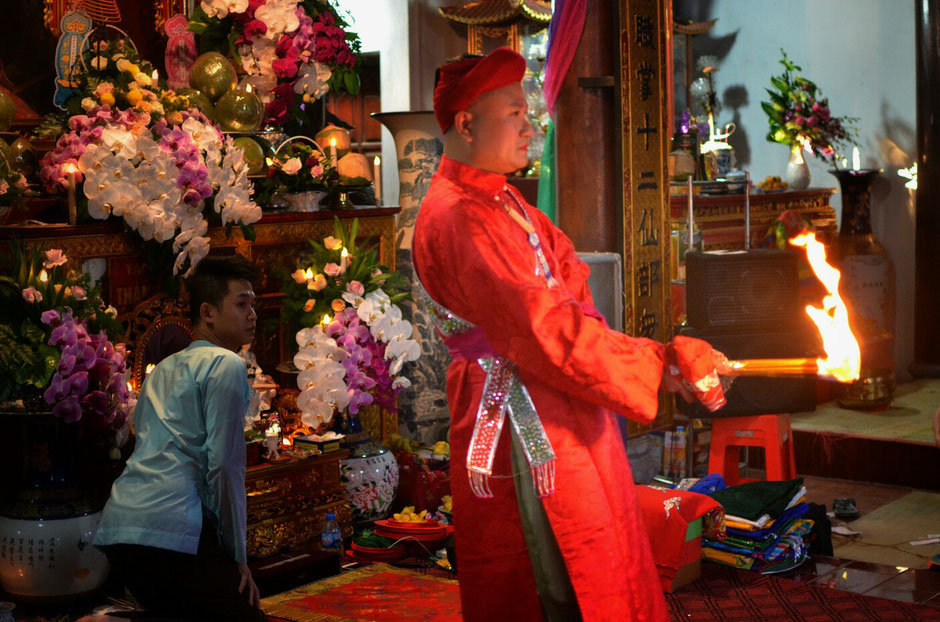 Len Dong – Zeremonie – Altar – geschmückt – Blumen – Gaben für die Geister – Person in prächtig roten Gewand – stehend – Feuerfackel in der Hand