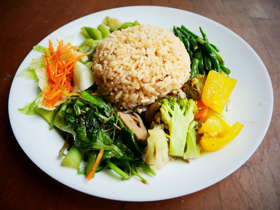 Organic brown rice with different types of chinese vegetables served on a simple white porcelain plate on a wooden table