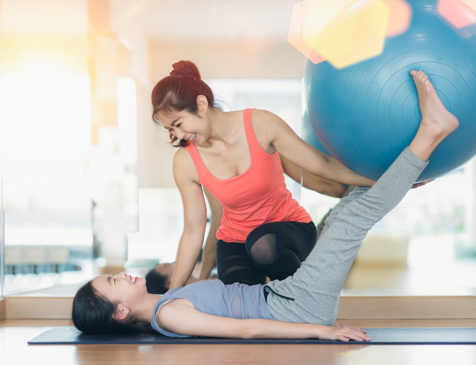 A female personal trainer assisting her female client in performing a corrective exercise with a swiss ball