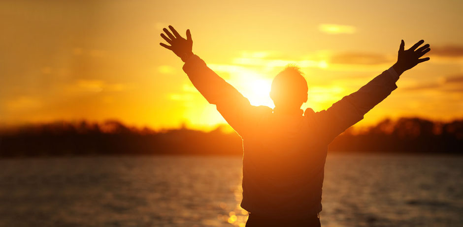 A silhouette of a man with his hands outstretched embracing the view of the sunrise