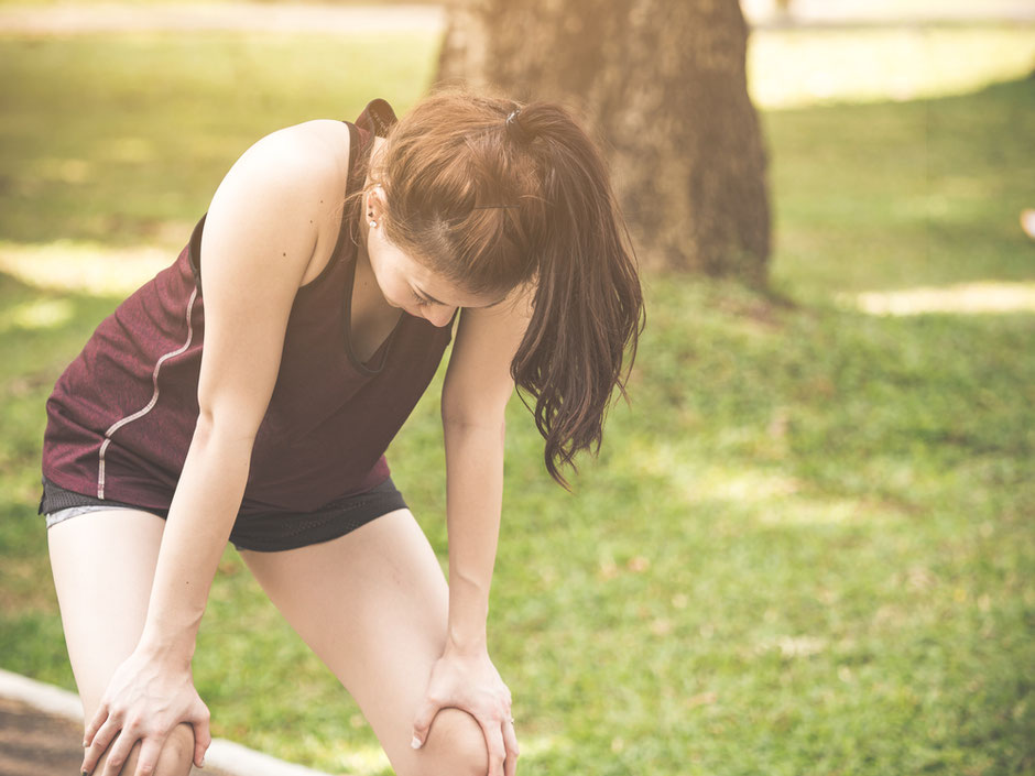 Woman at the park with her body bent forward and hands on her knees is exhausted from running