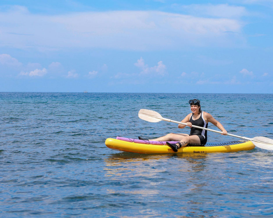 Frau auf einem SUP mit Paddel in der Hand auf offenem Meer