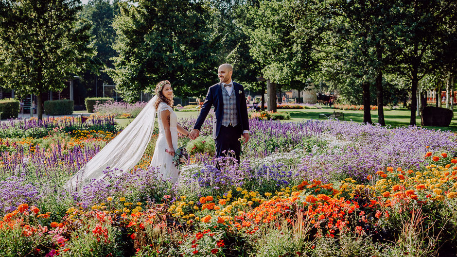 Braut und Bräutigam gehen Hand in Hand durch ein Blumenmeer bei Hochzeit in Kaiserslautern