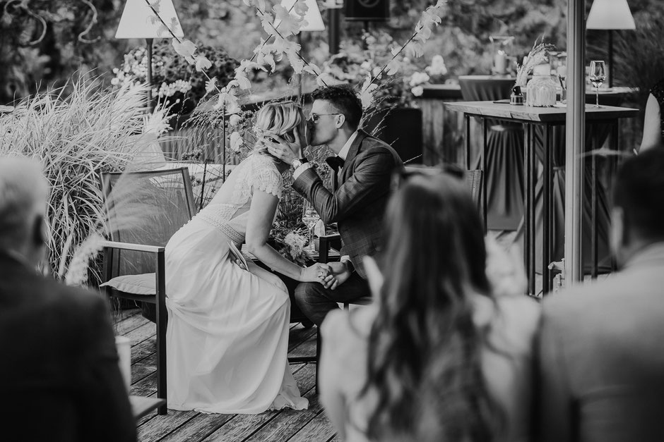 schwarzweisses Bild eines Brautpaars, dass sich gegenüber sitzt und küsst