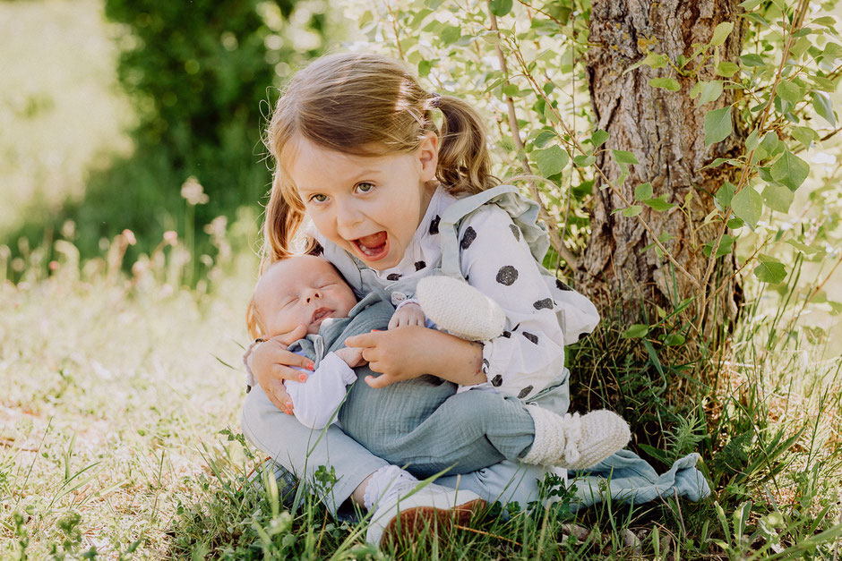 Schwester mit Baby auf dem Arm auf einer Wiese in Rheinhessen