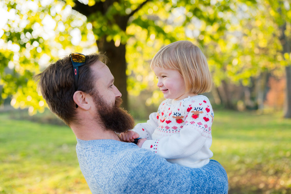 Bei einem Familien-Fotoshooting schauen sich Vater und Tochter froehlich an, dabei traegt er sie in seinen Armen. Ungestellte Familienfotos aus Duesseldorf und Duisburg.
