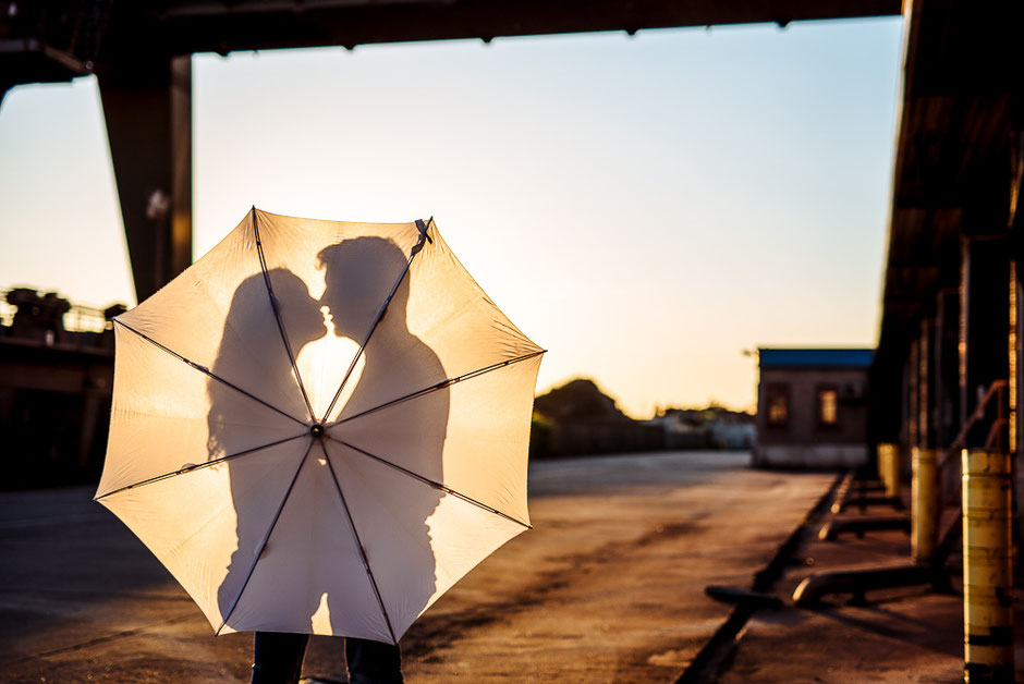 Der Schatten eines verliebten Paares faellt im Gegenlicht auf einen aufgespannten hellen Regenschirm.
