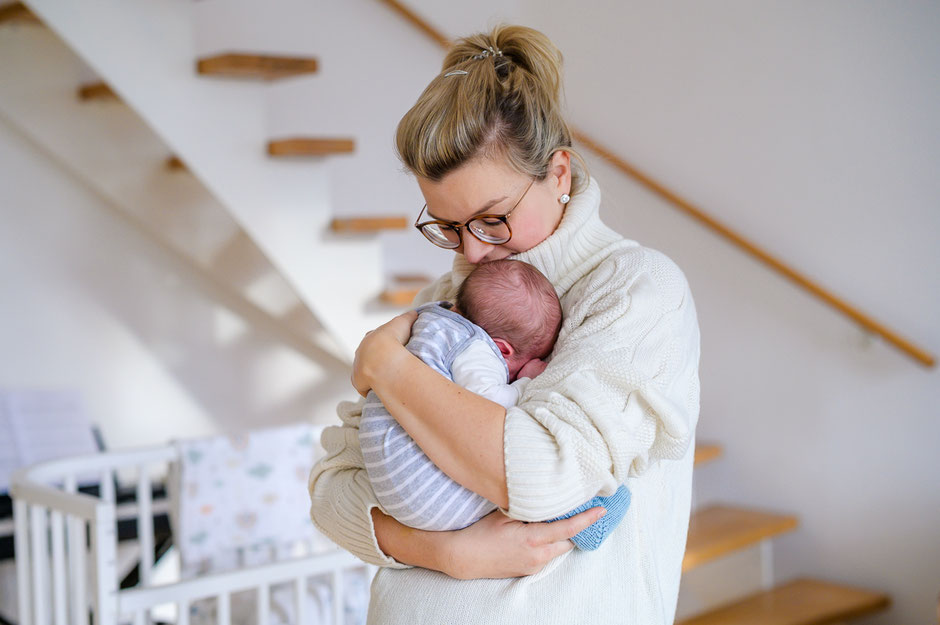 Liebevolle Mutter hält ihr neugeborenes Baby vor sich und genießt die erste gemeinsame Zeit.