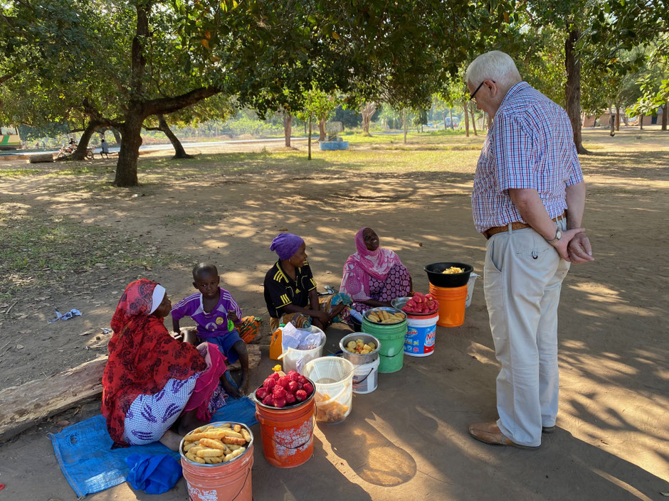 Afrikanische DDorfbewohner sitzen am Boden und verkaufen Ware. Vor ihnen steht Markus.