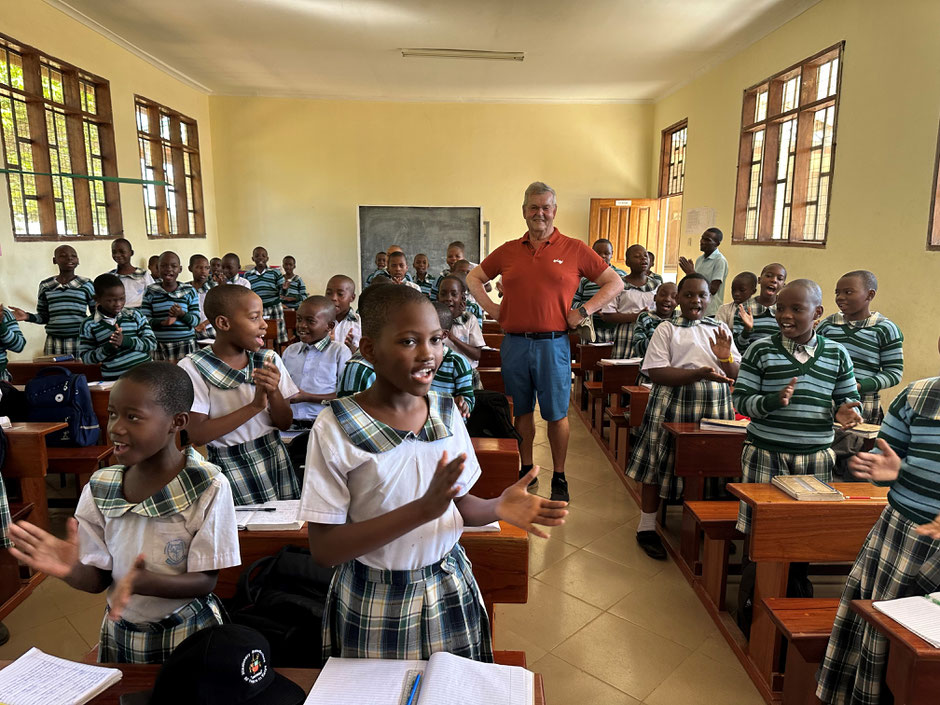 Kinder einer Schule in Ndana klatschen und singen im Unterricht. In der Mitte steht Franz Xaver Hirtreiter.