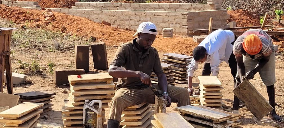 Drei Menschen die mit Holzteilen im Freien arbeiten. 