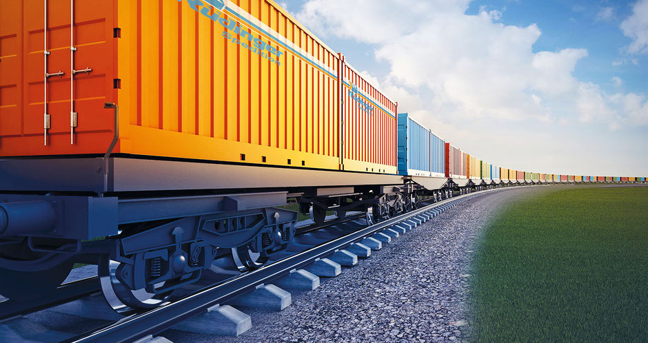 Es ist ein scheinbar unendlich langer Güterzug beladen mit Containern in einer langgezogenen Rechtskurve. Dominant in der linken Hälfte sind zwei orangene Rüdinger-Container auf der Ladefläche.