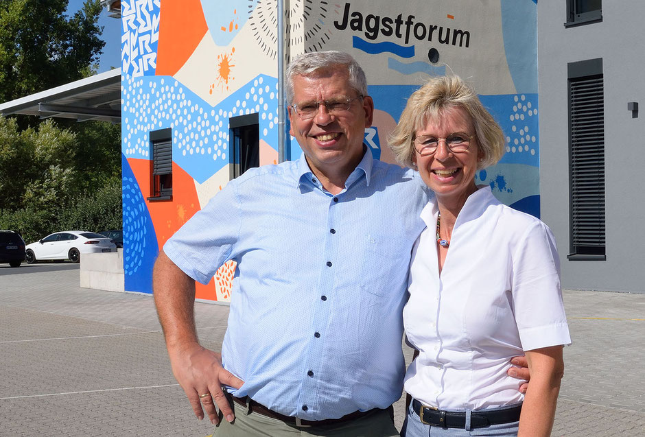 Man sieht Anja und Roland Rüdinger, sie steht rechts. Beide stehen vor dem Gebäude mit dem Jagstforum. 