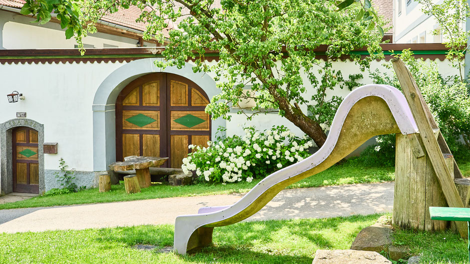 Eine Wellenrutsche steht im Garten vor dem Bauernhaus und ist erreichbar über eine kleine Holzleiter.