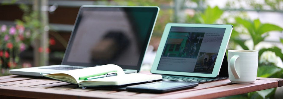 Laptop, Tablet, Notizbuch, Stift und Kaffeetasse zur Versicherung-Schadenbearbeitung
