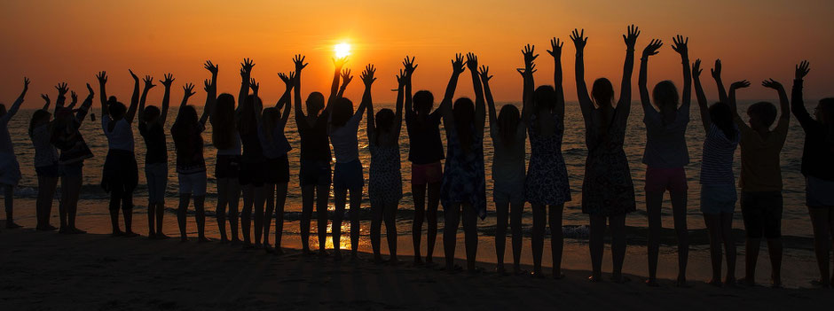 Silhouette von vielen Menschen am Strand in der Abendsonne 