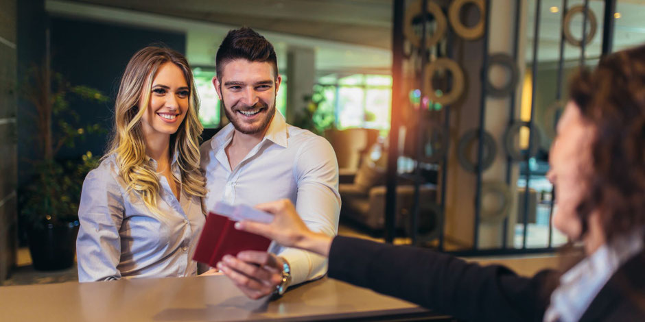 Paar auf Eventreise an der Hotel-Rezeption – abgesichert durch Ticket- und Reiserücktrittsversicherung