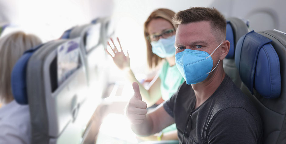 Corona-Urlaub: Frau und Mann im Flugzeug mit Maske auf dem Weg in den Urlaub. Was leistet die ERGO Reiseversicherung beim Ergänzungs-Schutz Covid-19?