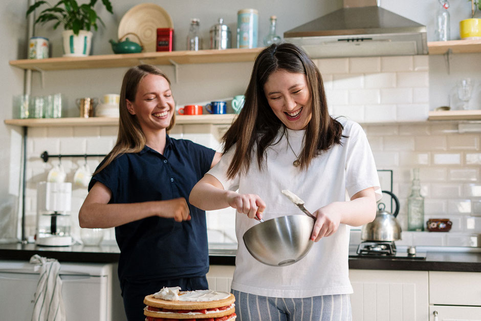 Zwei junge Frauen kochen gemeinsam in der Küche und haben Spaß