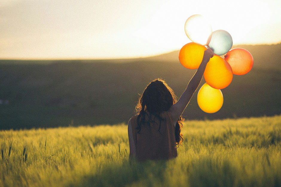 Eine Frau mit Luftballons in einem Kornfeld bei Abendlicht, als Symbol für "auf den Weg machen und Loslassen", Beweggründe, Anja Pries, Coaching, Supervision, Traumaberatung in Steinfurt