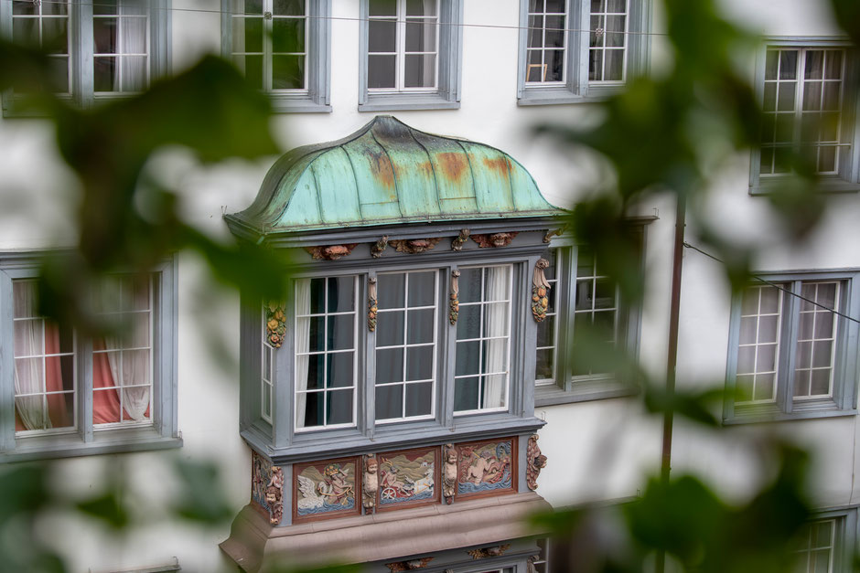 Historisches Haus mit kunstvoll bemaltem Erker und grün patiniertem Kupferdach in der Altstadt von St. Gallen. Detailreiche Fassadenmalereien und helle Fenster spiegeln die Verbindung von Tradition, Handwerk und Schweizer Baukultur – Blick aus dem HOZ Bac